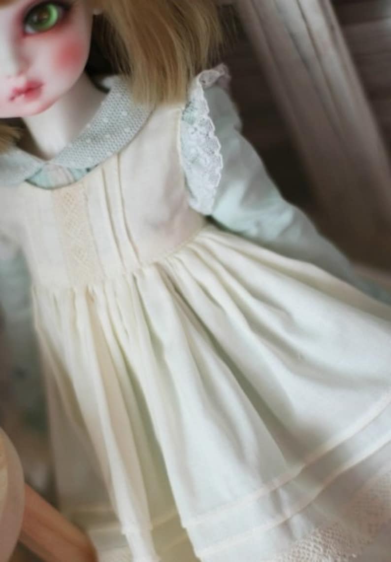 May include: A white dress with a lace trim and a green and white polka dot shirt underneath. The dress has a gathered skirt and a fitted bodice.
