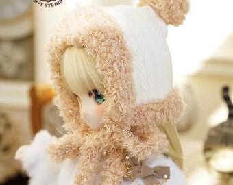 May include: A doll wearing a white knit hat with a tan pom-pom and trim, and a matching scarf. The doll has blonde hair and is wearing a white coat with a tan bow and pearl accents. The logo for M+Y Studio is visible.