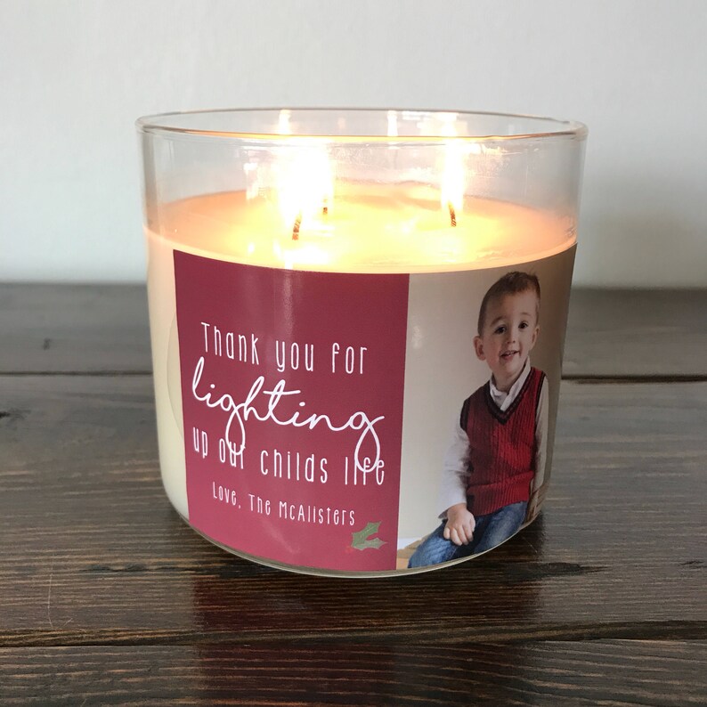 May include: A clear glass candle jar with a red and white label. The label has a photo of a young boy and the text "Thank you for lighting up our childs life Love, The McAllisters".
