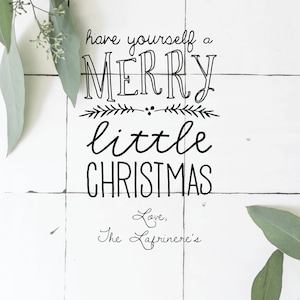 May include: A white tiled background with a handwritten message that reads "have yourself a merry little christmas Love, The Lafriniere's".  The message is surrounded by green eucalyptus leaves.