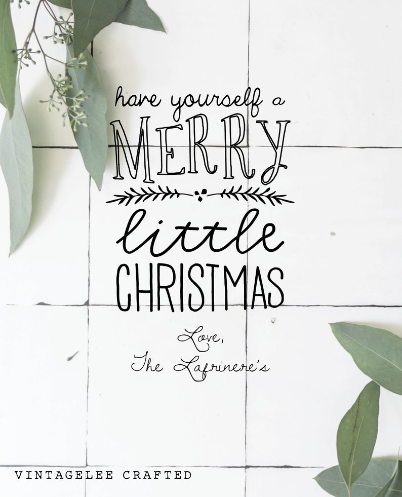 May include: A white tiled background with a handwritten message that reads "have yourself a merry little christmas Love, The Lafriniere's".  The message is surrounded by green eucalyptus leaves.