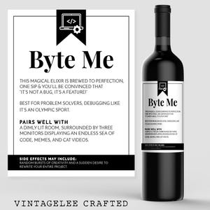 May include: A black wine bottle with a white label featuring the text "Byte Me" and a graphic of a laptop. The label also includes text about the wine's qualities and pairings. The bottle is part of the "Vintagelee Crafted" collection.