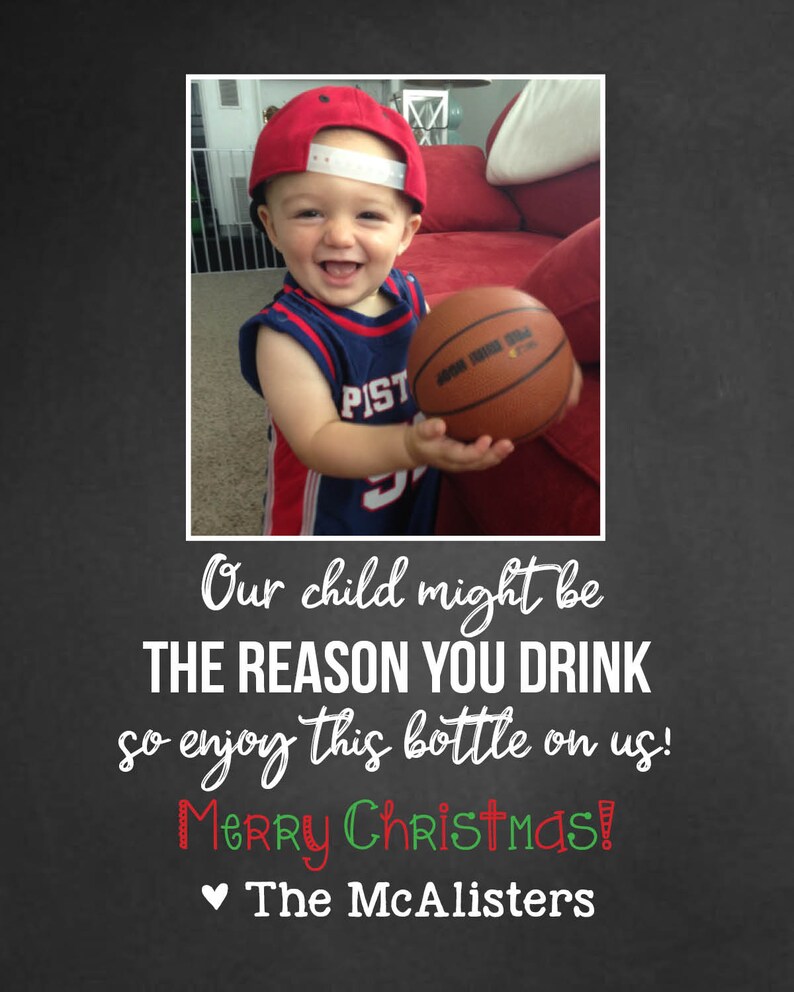 May include: A young child wearing a red baseball cap and a blue and white jersey holds a basketball. The text "Our child might be THE REASON YOU DRINK so enjoy this bottle on us! Merry Christmas! The McAlisters" is written below the image.