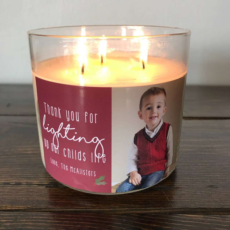May include: A clear glass candle jar with a red and white label. The label has a photo of a young boy and the text "Thank you for lighting up our child's life. Love, The McAllisters".