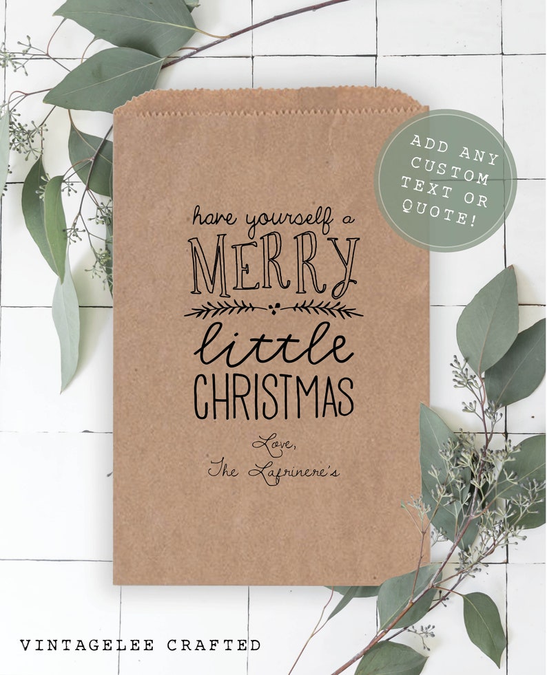 May include: A brown paper bag with a black printed design that says "have yourself a MERRY little CHRISTMAS" and "Love, The Lafrinere's". The bag has a white circle with black text that says "ADD ANY CUSTOM TEXT OR QUOTE!"