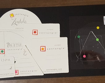 May include: A set of six white cards with black text and colored dots. The cards are labeled "Zentangle" and feature different geometric designs. The cards are on a black surface.