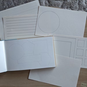 May include: A collection of white paper sheets and a notebook with various designs. The sheets include lined paper, dotted paper, and paper with geometric shapes. The notebook is open, displaying blank pages and geometric shapes.
