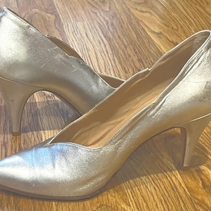 Op de afbeelding: Een paar zilveren pumps met hoge hakken. De schoenen zijn gemaakt van een glad, glanzend materiaal en hebben een spitse neus.