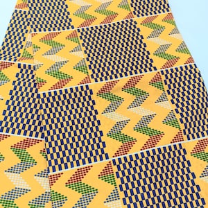 May include: A yellow fabric with a geometric pattern of blue, red, and green squares and triangles. The fabric is folded in half.