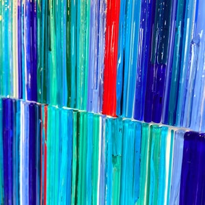 May include: Abstract art piece made of colorful glass rods in shades of blue, green, and red. The rods are arranged vertically and create a striped pattern.