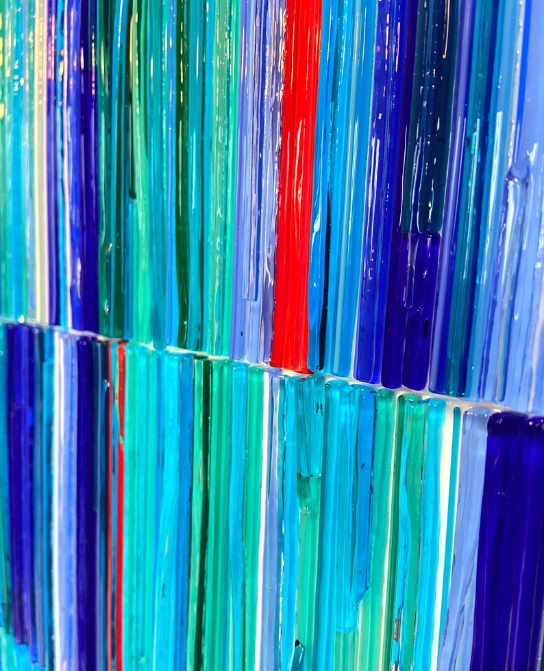 May include: Abstract art piece made of colorful glass rods in shades of blue, green, and red. The rods are arranged vertically and create a striped pattern.