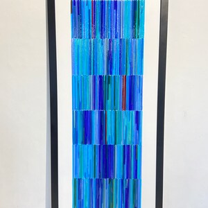 May include: A framed abstract art piece made of blue, green, and red glass rods. The rods are arranged in vertical lines, creating a textured and colorful pattern.