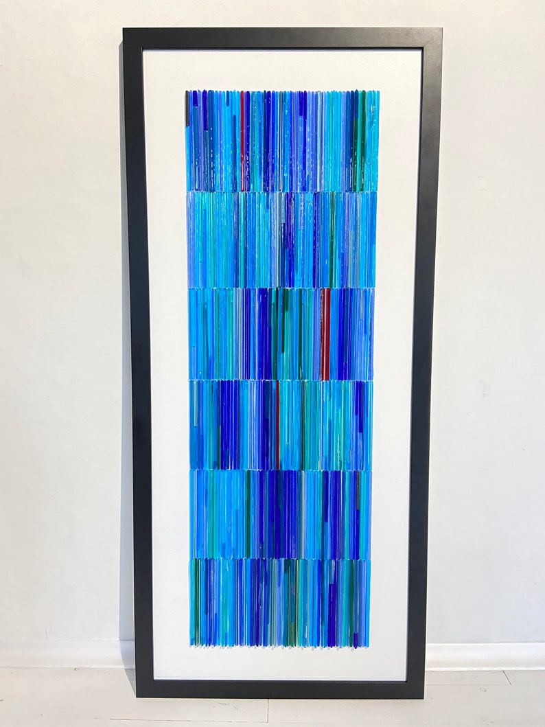 May include: A framed abstract art piece made of blue, green, and red glass rods. The rods are arranged in vertical lines, creating a textured and colorful pattern.