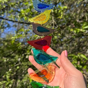 May include: A multi-coloured bird wind chime featuring six birds in shades of blue, yellow, brown, red, green, and orange. The birds hang from a silver chain, creating a decorative garden ornament.