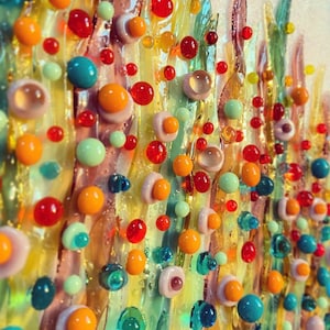 Könnte beinhalten: Nahaufnahme eines bunten Mosaik-Kunstwerks mit verschiedenen Farbtönen von Gelb, Grün, Rot, Orange und Rosa. Das Mosaik besteht aus kleinen, runden Glasstücken, die in einem zufälligen Muster angeordnet sind.
