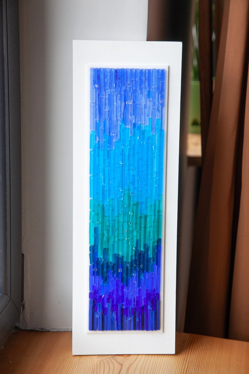 May include: A rectangular wall art piece featuring a gradient of blue and teal glass rods set in a white frame. The artwork transitions from deep indigo at the bottom to lighter shades of blue at the top, creating a visual flow.