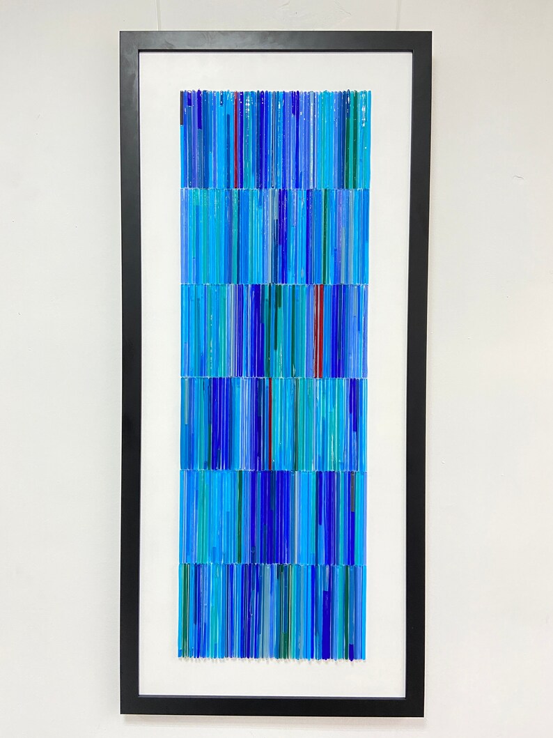 May include: A framed artwork made of blue, green, and red glass rods arranged in a vertical pattern.