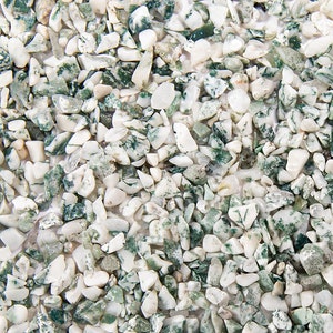 May include: Close-up of a collection of small, irregularly shaped stones. The stones are primarily white with patches of green, creating a speckled appearance. The image has a natural, earthy aesthetic, with the "happy nook shop" logo in the bottom right corner.