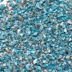 May include: A close-up view of a large quantity of small, blue-green, irregularly shaped, and translucent gemstone chips. The chips are scattered across a white surface. The image includes a small, round, white logo with the text "happy nook shop" in black.