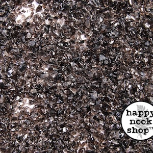 Pode incluir: Uma imagem de close-up de um monte de pequenos pedaços de vidro marrom escuro. Os pedaços de vidro são irregulares em forma e tamanho, e têm um brilho ligeiramente iridescente. Os pedaços de vidro estão espalhados sobre um fundo branco.