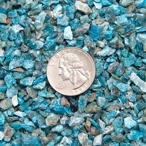 May include: A close-up of a pile of small, blue-green gemstones. A US quarter is placed on top of the gemstones for scale.