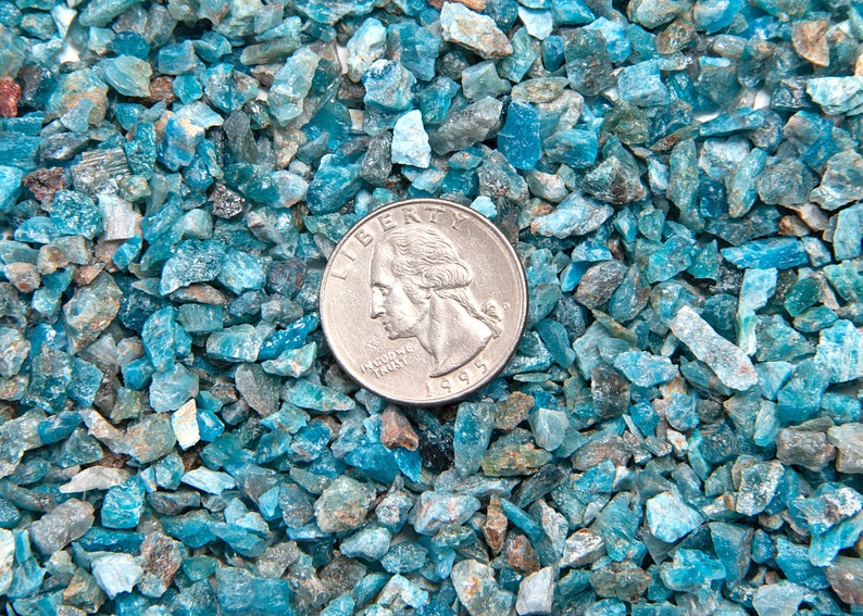 May include: A close-up of a pile of small, blue-green gemstones. A US quarter is placed on top of the gemstones for scale.