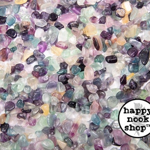 May include: A close-up image of a large quantity of small, colorful fluorite tumbled stones. The stones are a mix of purple, green, blue, and yellow.