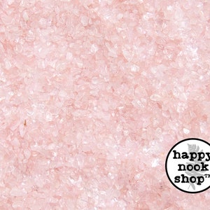 May include: A close-up view of a large quantity of small, light pink rose quartz chips. The chips are irregularly shaped and have a translucent appearance. The image is taken from a bird's eye view.