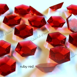 May include: Ruby red candy shaped like gemstones, scattered on a white surface. The candy is labeled "A Pocket Full of Sweets".