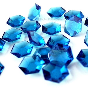 Peut inclure: Des bonbons bleus facett&eacute;s en forme d'hexagone avec un sommet pointu, &eacute;parpill&eacute;s sur une surface blanche.