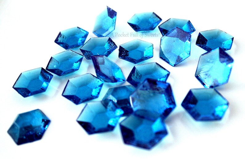 Peut inclure: Des bonbons bleus facett&eacute;s en forme d'hexagone avec un sommet pointu, &eacute;parpill&eacute;s sur une surface blanche.