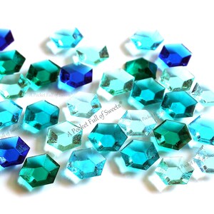 Peut inclure: Une collection de pierres pr&eacute;cieuses en verre facett&eacute;es bleues, bleu-vert et vertes. Les pierres pr&eacute;cieuses sont de forme hexagonale et de tailles vari&eacute;es. Les pierres pr&eacute;cieuses sont &eacute;parpill&eacute;es sur un fond blanc.