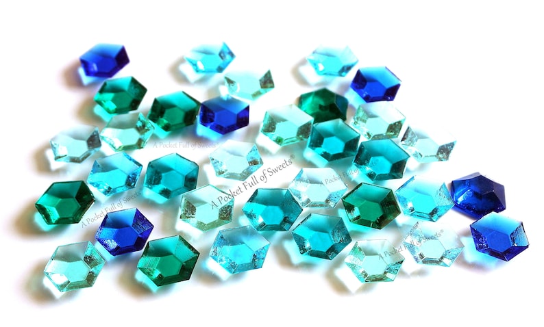 Peut inclure: Une collection de pierres pr&eacute;cieuses en verre facett&eacute;es bleues, bleu-vert et vertes. Les pierres pr&eacute;cieuses sont de forme hexagonale et de tailles vari&eacute;es. Les pierres pr&eacute;cieuses sont &eacute;parpill&eacute;es sur un fond blanc.
