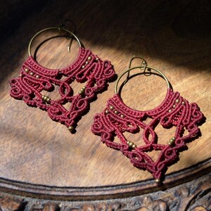 May include: A pair of maroon crocheted earrings with gold beads hanging from brass hoops.