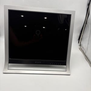 May include: A Sony computer monitor featuring a sleek silver frame and a black screen. The display is mounted on a wide, integrated silver stand that provides a stable base. The Sony logo is printed in small, subtle lettering on the bottom bezel.