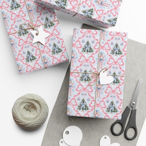 Puede incluir: Varios regalos envueltos con papel de regalo azul claro con un patrón de lazos rosas, árboles de Navidad y cascanueces. Los regalos están atados con hilo y adornados con etiquetas de papel blanco. También se ven una madeja de hilo y unas tijeras.