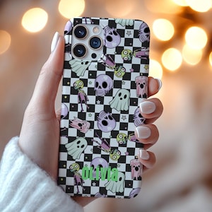 May include: A black and white checkered phone case featuring a repeating pattern of purple skulls, ghosts, zombies, and candles. The name "Olivia" is printed in green on the case.