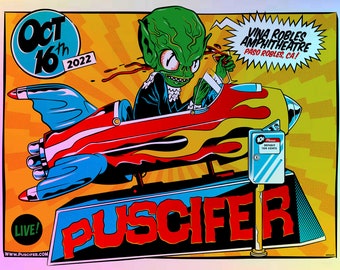 May include: A concert poster for the band Puscifer, featuring a green alien character driving a rocket-shaped car. The poster is yellow, red, and blue with the text "Oct 16th 2022" and "Vina Robles Amphitheatre Paso Robles, CA!" The poster also includes the text "Puscifer" and "Live!" with the website www.puscifer.com.