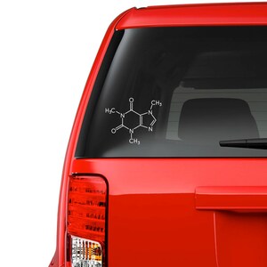 Op de afbeelding: Witte sticker van het cafe&iuml;nemolecuul op de achterruit van een rode auto. De chemische structuur wordt weergegeven in een eenvoudig, strak ontwerp, perfect voor wetenschapsliefhebbers en koffiedrinkers.