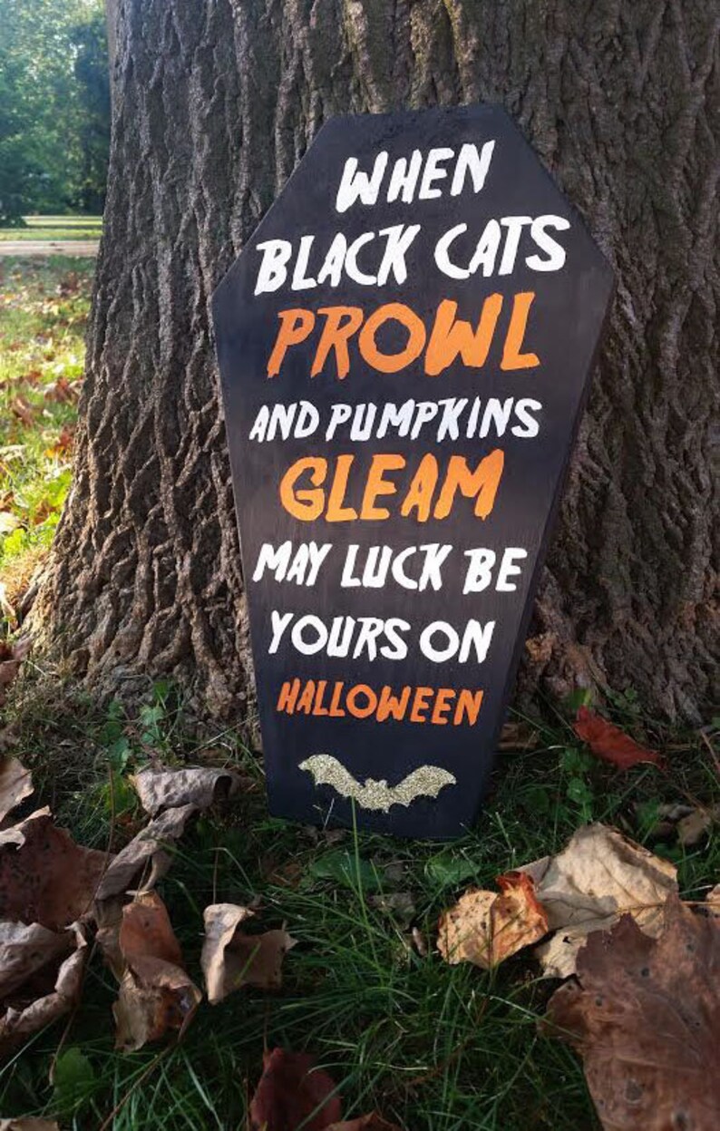 May include: Black coffin-shaped Halloween sign with white and orange text: "When black cats prowl and pumpkins gleam, may luck be yours on Halloween." A glittery bat is at the bottom.