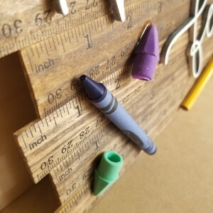 May include: Wooden ruler-style growth chart with inch measurements and a decorative "hello" sign. Includes a blue crayon, a yellow pencil, and two erasers. The wooden chart has a natural wood grain finish.