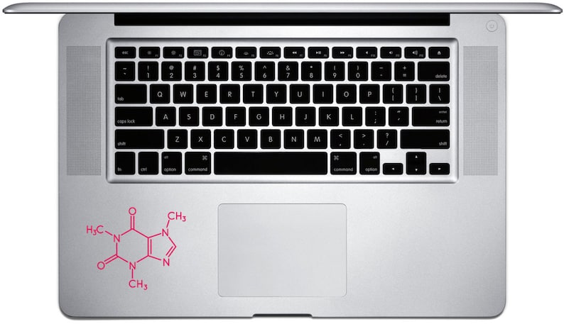 Op de afbeelding: Een zilveren laptop met een zwart toetsenbord en een roze sticker van een cafe&iuml;nemolecuul op de polssteun. De laptop is open en toont het toetsenbord en het touchpad. De sticker is een gestileerde chemische structuur.