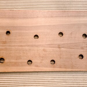 May include: A rectangular wooden board with eight evenly spaced circular holes. The board is made of light brown wood and has rounded corners. The holes are evenly spaced across the surface.
