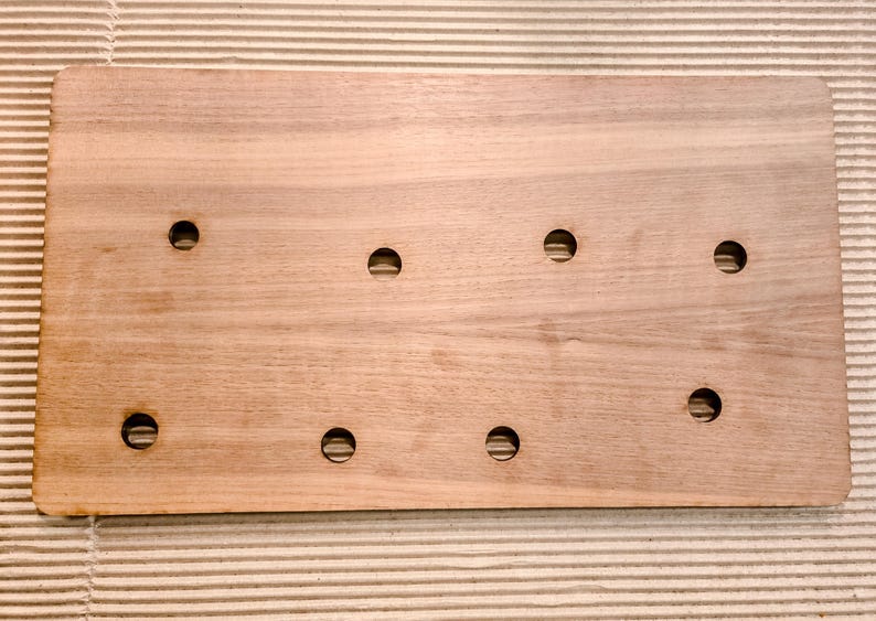May include: A rectangular wooden board with eight evenly spaced circular holes. The board is made of light brown wood and has rounded corners. The holes are evenly spaced across the surface.
