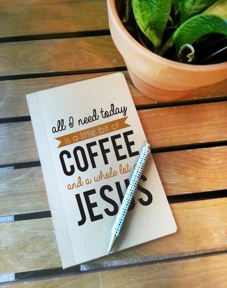 May include: A notebook with the text "all I need today is a little bit of COFFEE and a whole lot of JESUS" and a pen with a white and black polka dot design. The notebook and pen are on a wooden surface, with a potted plant in the background.