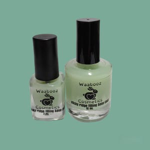 May include: Two bottles of Waabooz Cosmetics sticky ridge filling base coat. One bottle is 7 mL, the other is 15 mL. Both bottles are clear with a light green liquid and a black cap. The Waabooz logo is a bunny with a heart.