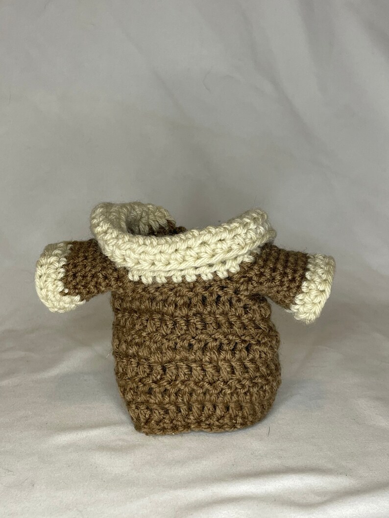 K&ouml;nnte beinhalten: Ein brauner H&auml;kelpullover mit einem wei&szlig;en H&auml;kelrand um die Kapuze und die &Auml;rmel.