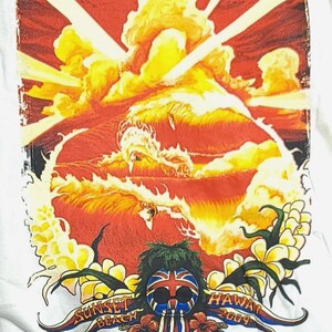 May include: White t-shirt featuring a vibrant graphic of a sunset scene with a large wave and a stylized face with sunglasses and a Union Jack design. The text "Sunset Beach Hawaii 2009" is also included.