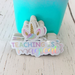 May include: A stack of iridescent stickers with a unicorn and the text "TEACHING IS magical".