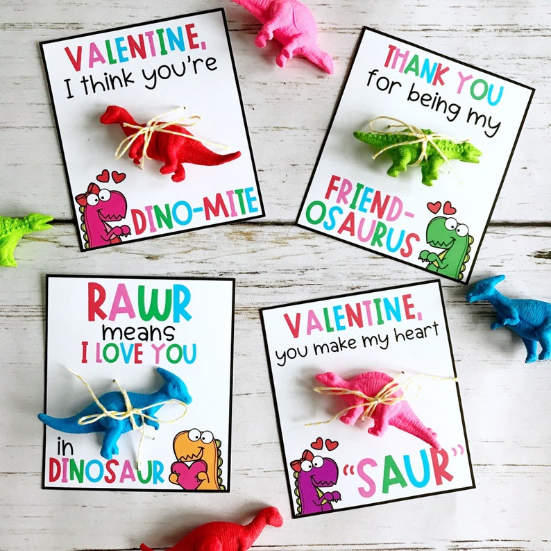 May include: Four Valentine's Day cards with dinosaur-themed puns. Each card features a different dinosaur toy and a Valentine's Day message. The messages include "I think you're dino-mite", "Thank you for being my friend-osaurus", "Rawr means I love you in dinosaur", and "Valentine, you make my heart "saur"".